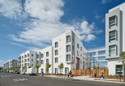 Large white building with gray bays, sunshades, and open-air circulation against blue sky