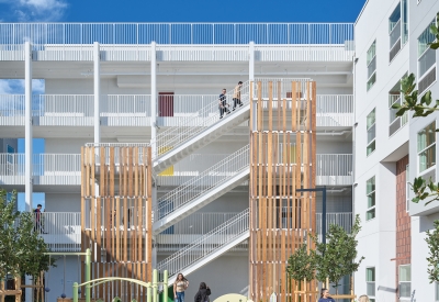 View of courtyard play structure and wood-lined stair tower of large white building against bright blue skyains