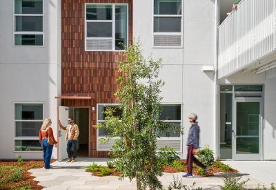 Apartment entry with two people talking viewed from a courtyard with hexagonal concrete tiles and log benches