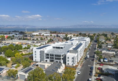 Aerial view of large white building set in an urban context showing entry to multilevel parking garage