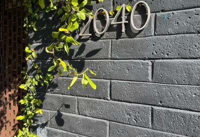 Black brick wall with plantings slightly obscuring metal building number 2040 in a san serif font