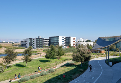 Large gray and white building with park and bike path in foreground and blue sky