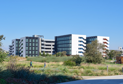 Large gray and white building against blue sky with park and bike path in foreground 