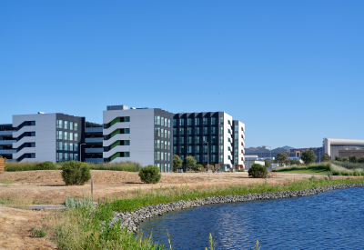 Large gray and white building against blue sky with a lake in foreground 