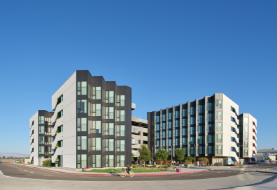 Large gray and white building with park and bike path in foreground and blue sky