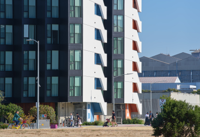 Large gray and white building with park and bike path in foreground and blue sky
