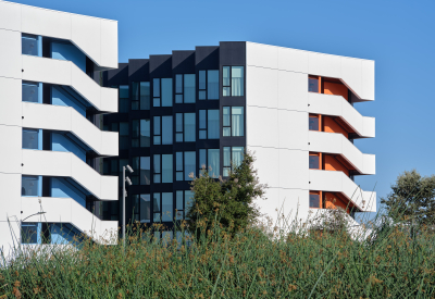 Gray and white building with orange and light blue accents against blue sky and green landscape in the foreground