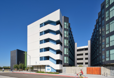 Large gray and white building with bike path in foreground and blue sky
