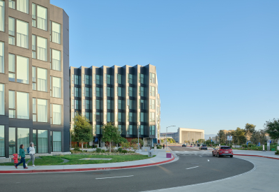 Gray buildings against a blue sky with cars on road in front