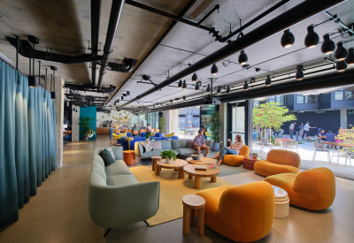 Lounge area with blue sofas, orange chairs and a blue curtain looking to outdoor space through open garage doors