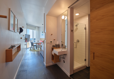 Interior suite with seating area and sliding door in background and white bathroom sink and shower in foreground