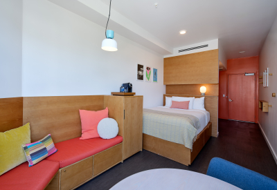 Bedroom studio with built in wooden bed and seating area with red cushion  