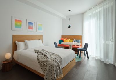 White bedroom with wooden built in seating and round table in background and three framed prints above a wood bed