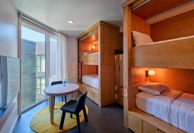 Bedroom with four wooden built-in bunk beds, yellow rug and large window