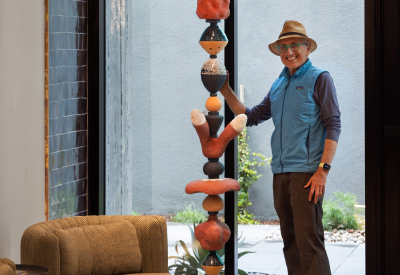 Man in hat and blue vest posing with ceramic sculpture