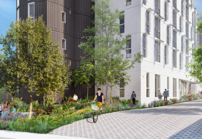 Woman on bicycle in front of gray and white building and garden plants