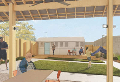 Man sitting under pavilion shelter with grass and small building in background