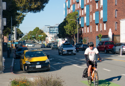 Red brick apartment building with cyclist and taxi in foreground