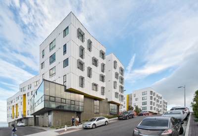 Street view of white apartment building with cars and pedestrians