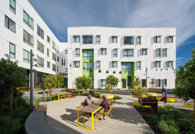 Exterior of white apartment building with green entry portals; seating in foreground