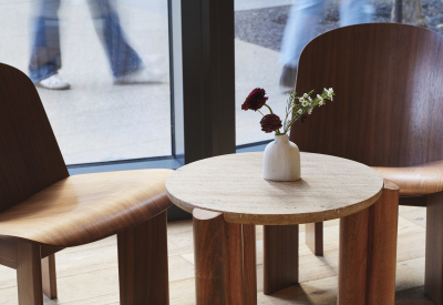 Detail shot of two chairs and a low table in front of window; passersby visible outside