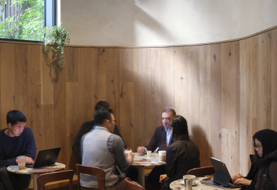 People having coffee and working on laptops at tables along the curving wood wall