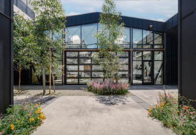View of building with black steel framing and glass from a gravel courtyard