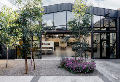 Steel frame building with open garage door and glass and small trees in the foreground courtyard 