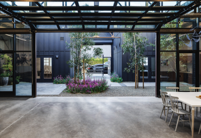 Large black steel framed room with glass and garage door opening to courtyard with trees