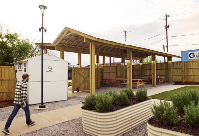 A man in a checked shirt and jeans walks past raised garden beds