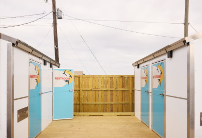Two small structures with four doors marked with restroom signs share a wooden deck