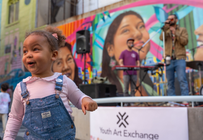 Young girl in courtyard in front of musicians and colorful mural