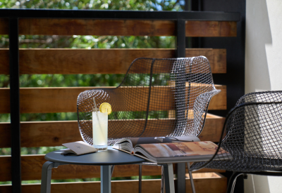 Closeup shot of a glass of lemonade with a lemon slice on a shady balcony with a wire chaire
