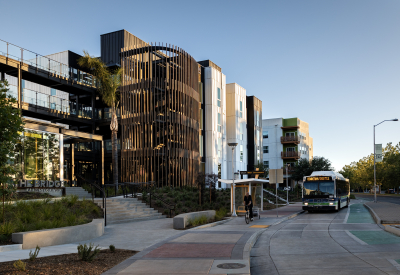 Multifamily building with rounded wood-slatted stair tower, with bus at bus stop in front