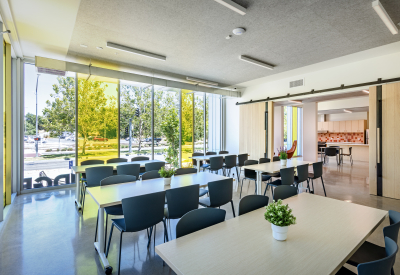 Interior of a community room with conference tables and chairs and a floor-to-ceiling window with clear and yellow glass