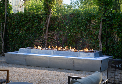 Sculptural concrete and steel fire feature with flames in front of ivied wall