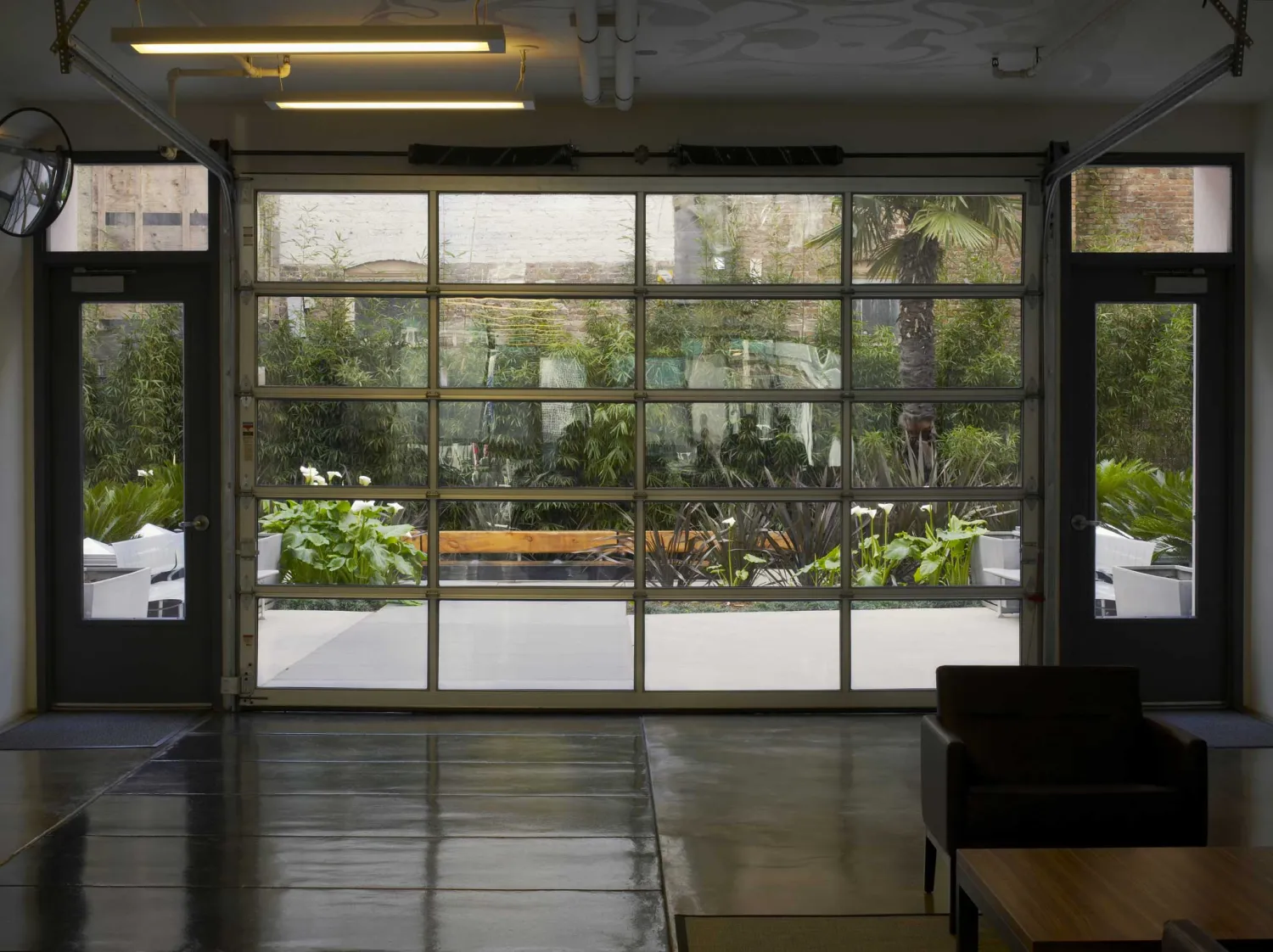 View from the lobby through a glass roll-up garage door into the planted courtyard.