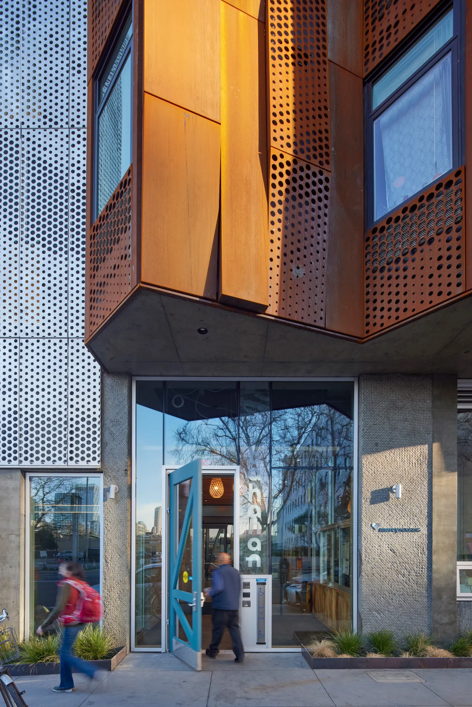 Closeup of entry at Tahanan Apartments showing weathering-steel and aluminum facade and custom blue front door.