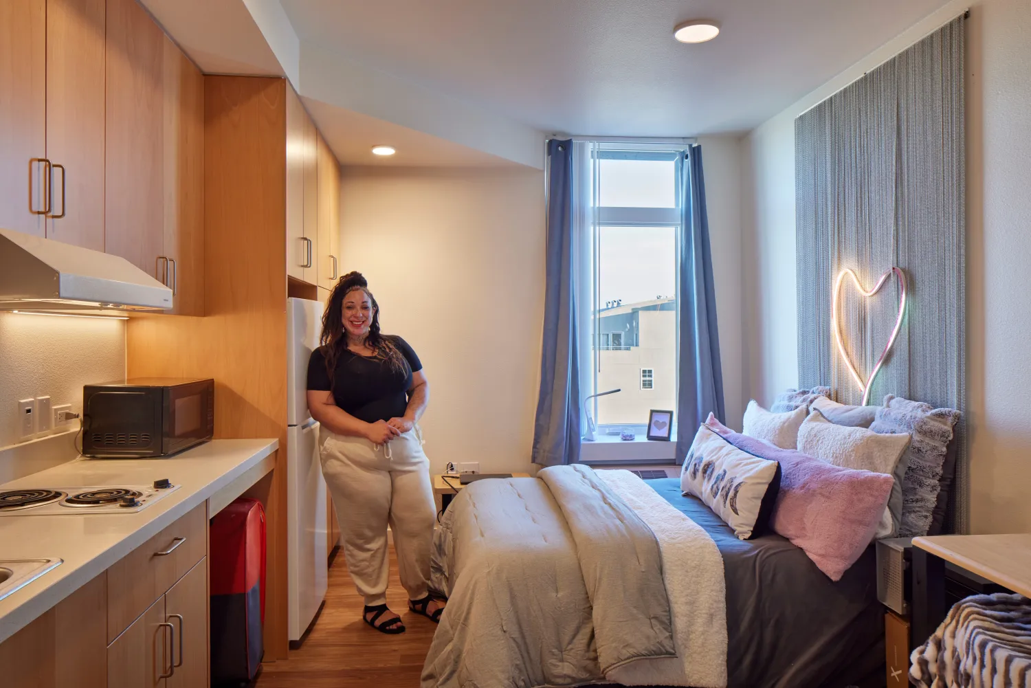 Interior of studio unit with resident showing kitchen and bed set-up.