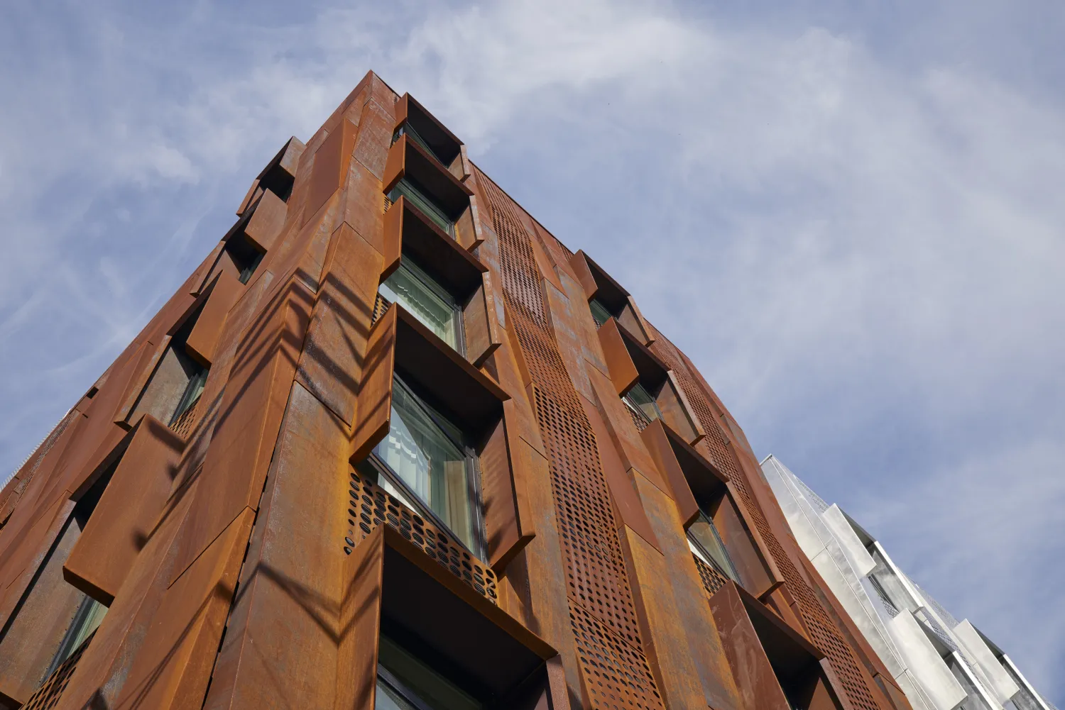 Detail of weathering steel rainscreen at corner, with clouded blue sky.