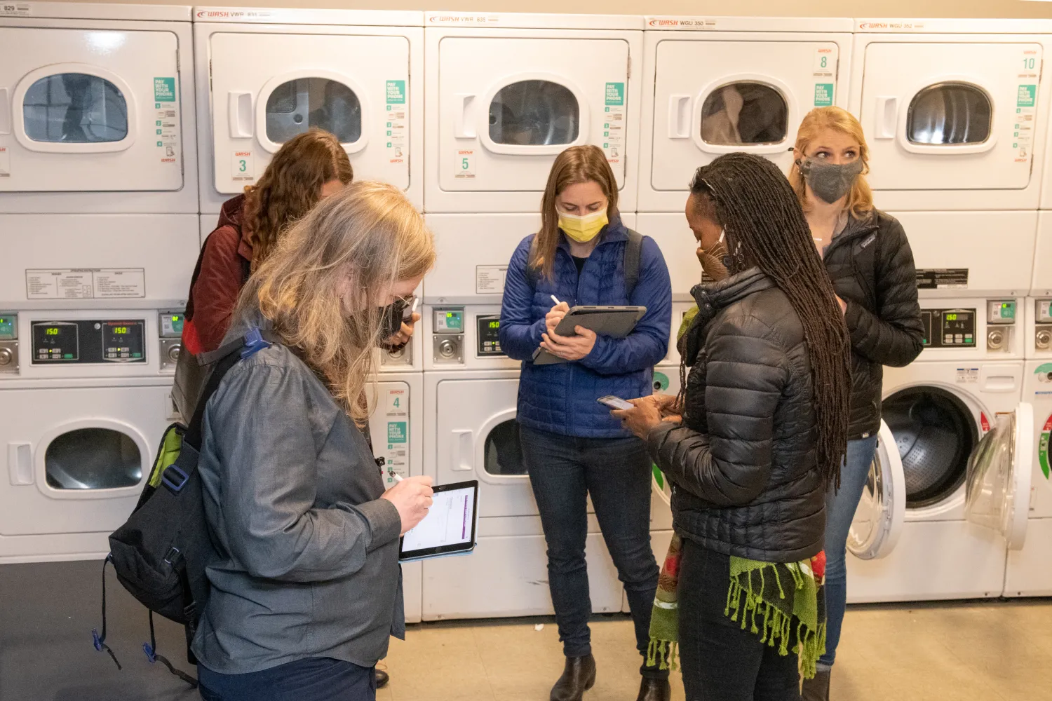 Principal Katie Ackerly and others standing and taking notes in the Laundry Room of a building.
