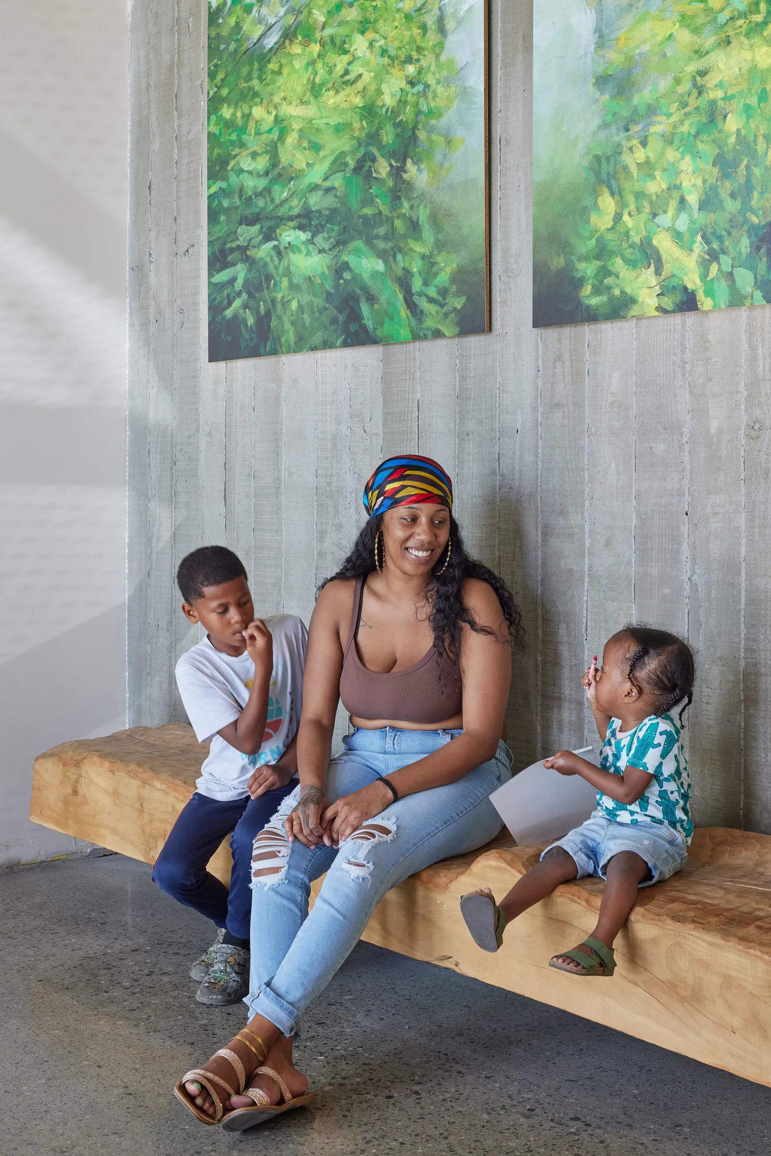 Woman and two children sitting on a bench inside the lobby of Coliseum Place in Oakland, California.