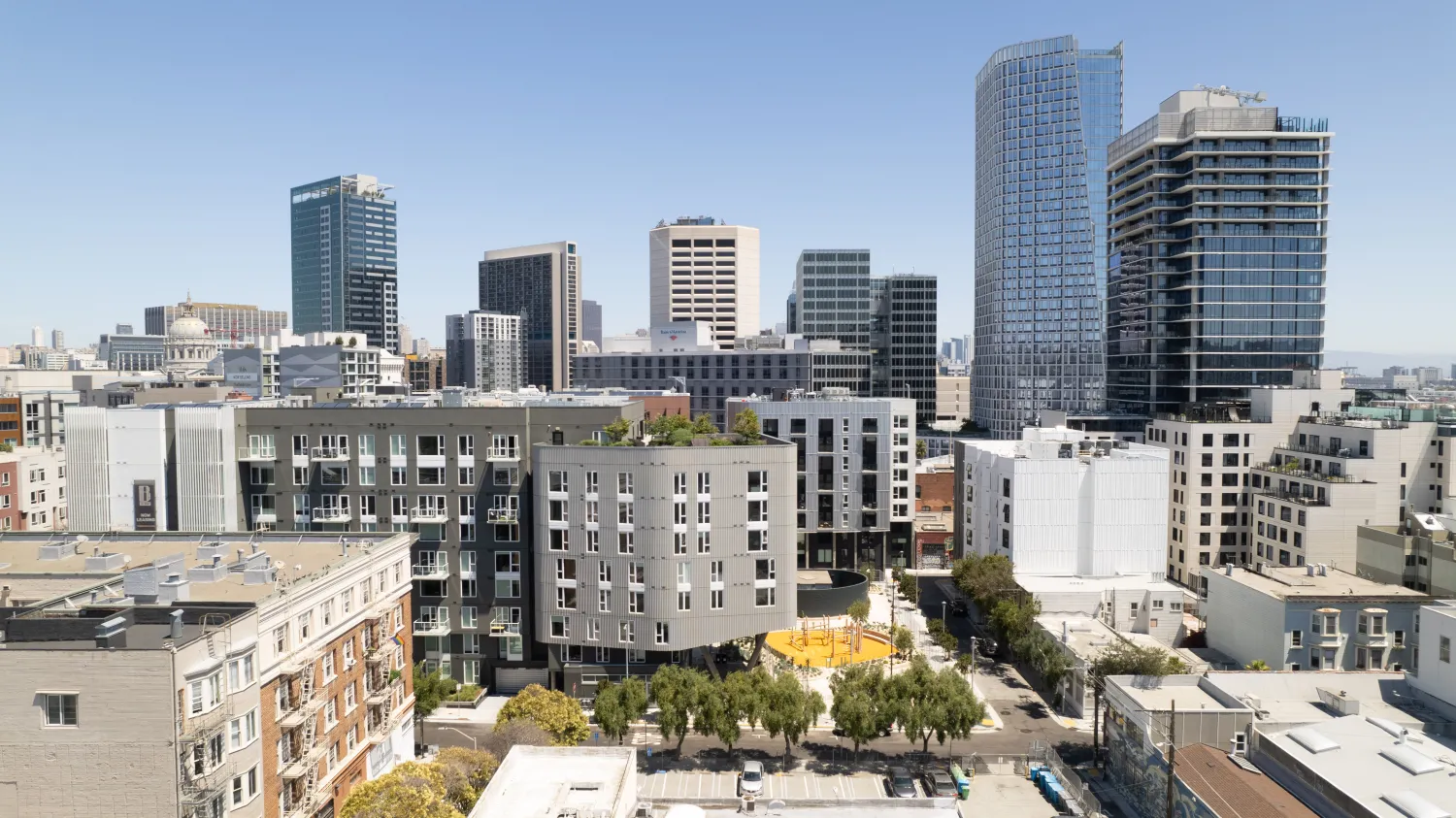 Aerial view of diverse buildings centered around a landscaped urban park with blue sky in background.
