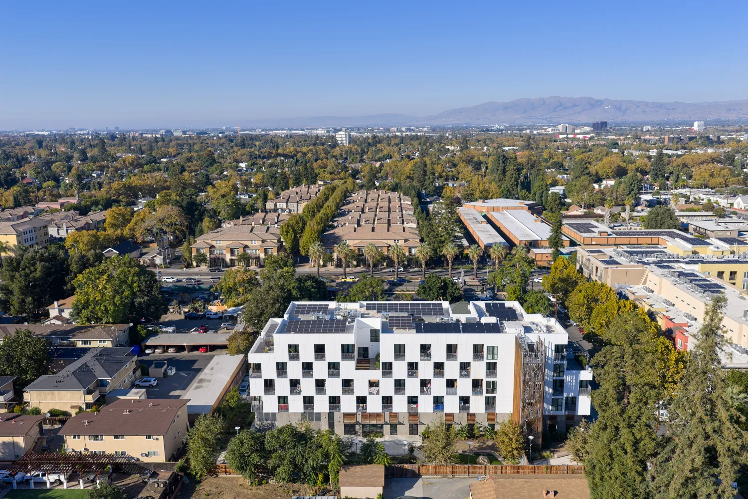 Aerial view of courtyard side of white apartment building in cityscape with hills and blue sky in background