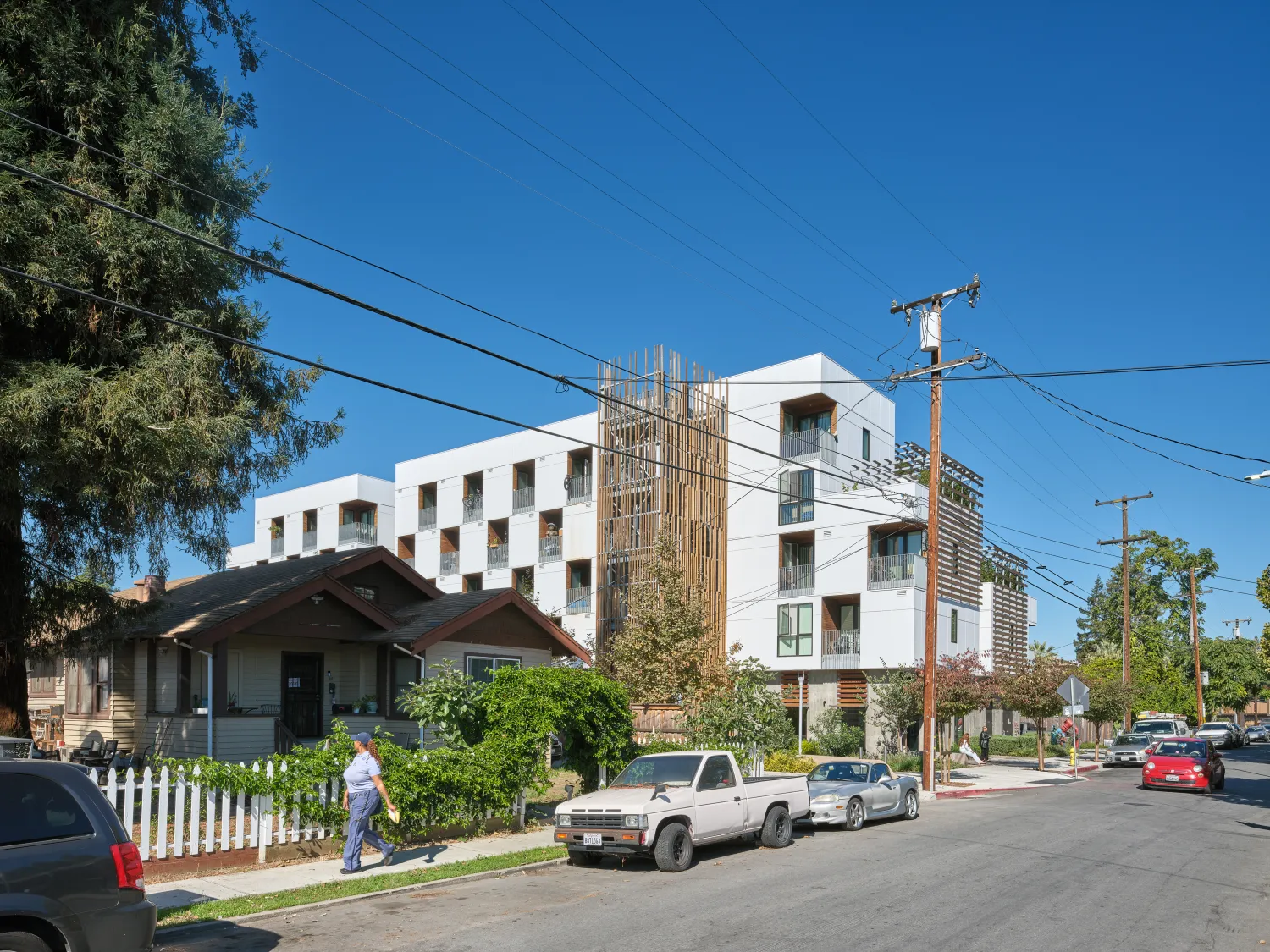 Street level view of white apartment building with wood stair tower next to single family home