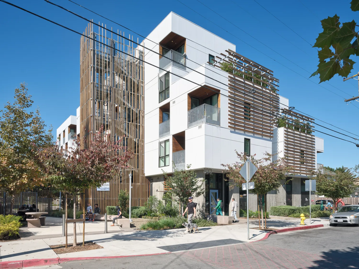 Corner view of white apartment building with wooden stair tower, trellises, and blue front door