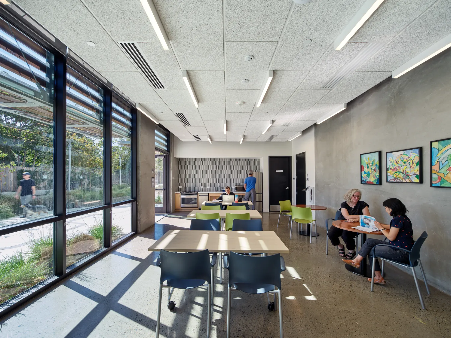 Interior of community room with glass wall at left and people sitting and reading