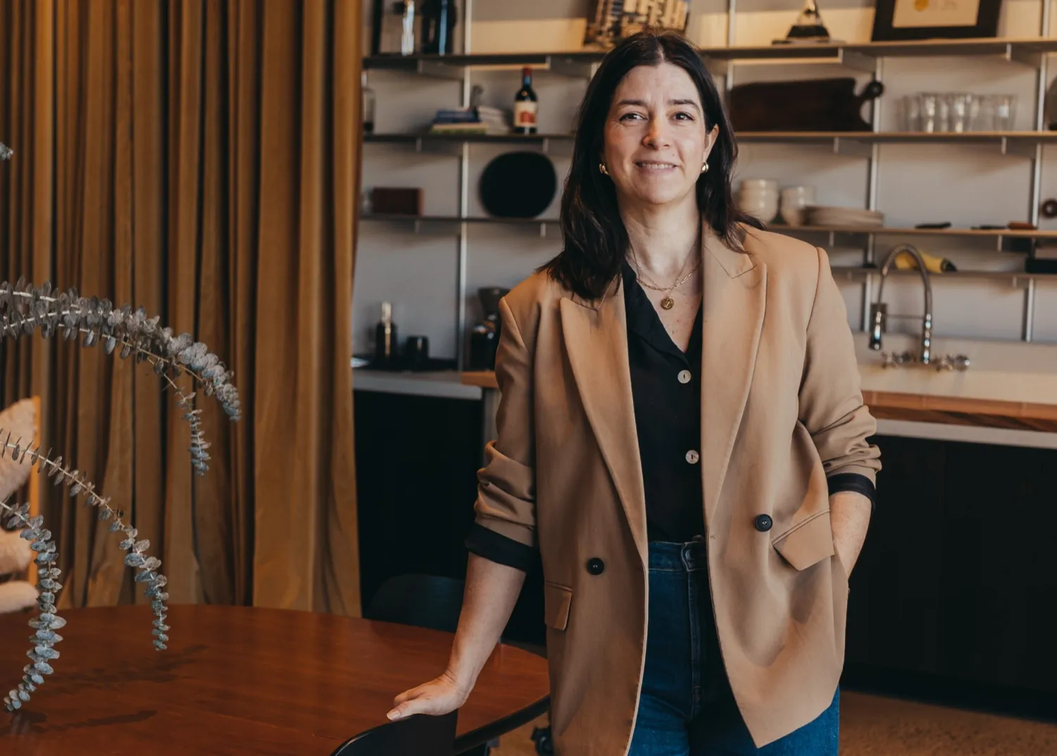 Woman in tan blazer standing beside table