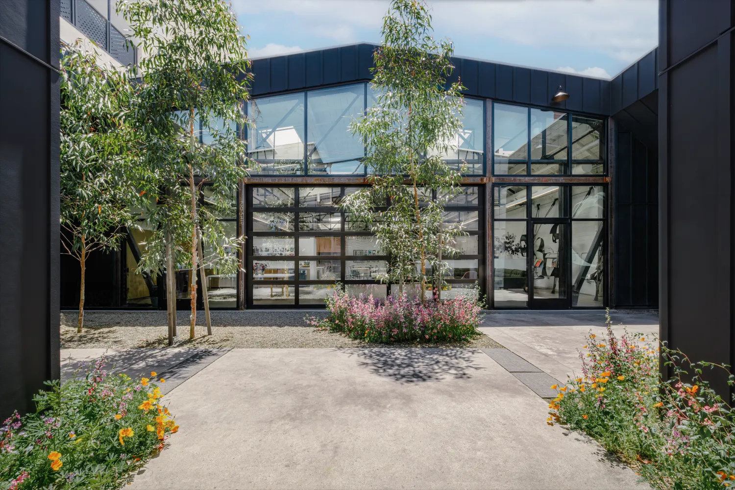 View of building with black steel framing and glass from a gravel courtyard