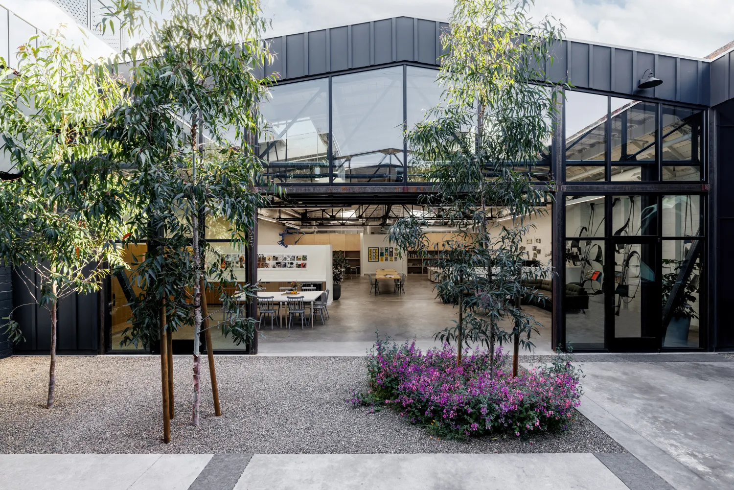 Steel frame building with open garage door and glass and small trees in the foreground courtyard 